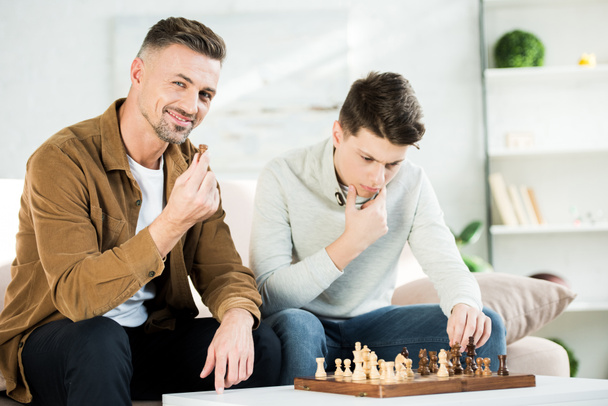 pensive father and teen son playing chess in living room - Fotoğraf, Görsel