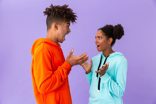Photo of unhappy african american brother and sister standing together and arguing isolated over violet background - Foto, Imagem