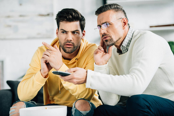 serious son and mature father watching tv together on weekend at home - Photo, Image