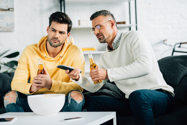 son and mature father watching tv with beer on weekend at home - Photo, Image