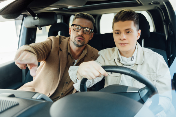 όμορφος πατέρας δείχνει σε κάτι ενώ διδάσκει έφηβος γιος οδήγηση αυτοκινήτου - Φωτογραφία, εικόνα