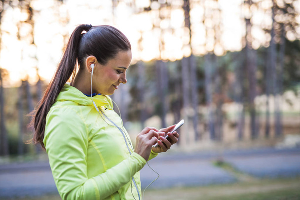 Smartphone kullanarak bir genç kadın atlet açık havada sonbahar doğada. - Fotoğraf, Görsel