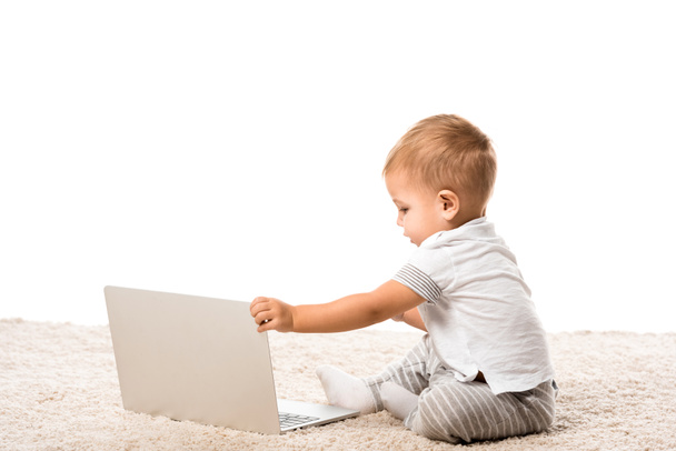 totyogó fiú ül a szőnyegen elszigetelt fehér laptop - Fotó, kép