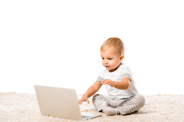 smiling toddler boy sitting with laptop on carpet isolated on white - 写真・画像