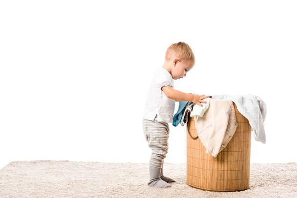 bambino ragazzo in piedi davanti a cesto di vimini lavanderia su tappeto isolato su bianco
 - Foto, immagini