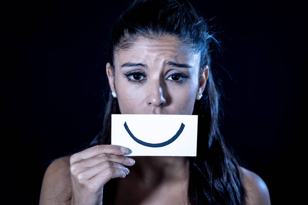 dramatische Nahaufnahme Porträt einer traurigen Frau, die ihre Depression versteckt mit einem Lächeln, das auf Papier gemalt wurde, in menschlicher Emotion leidet, in Stille Depression Konzept isoliert auf schwarzem Hintergrund. - Foto, Bild