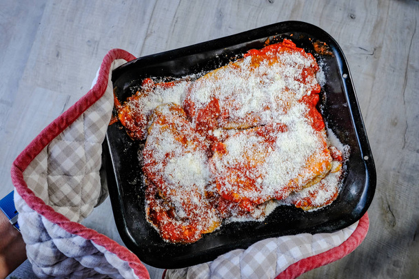 rohes Gericht aus Aubrgine Parmigiana, das in einem Ofenhandschuh gehalten wird und bereit ist, in den Ofen zu schlüpfen, um zu kochen. - Foto, Bild