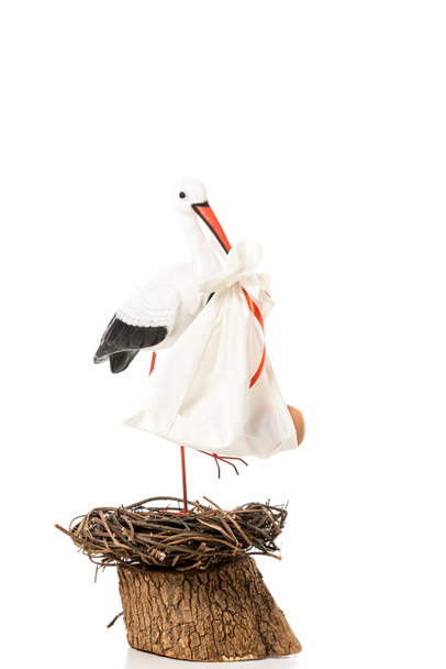 декоративний лелека, що тримається в дзьобному дитячому підгузку і стоїть у плетеному гнізді ізольовано на білому
 - Фото, зображення