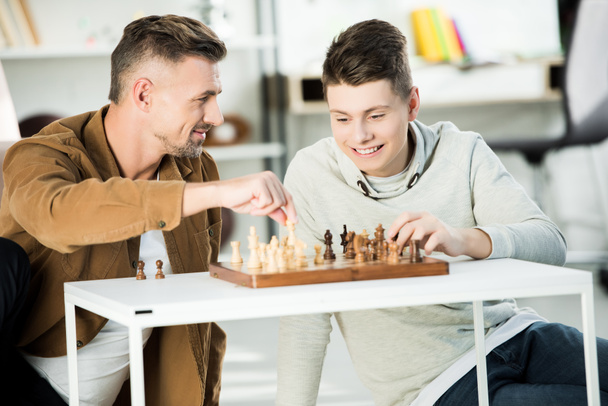 happy father and teen son playing chess together at home - Фото, зображення