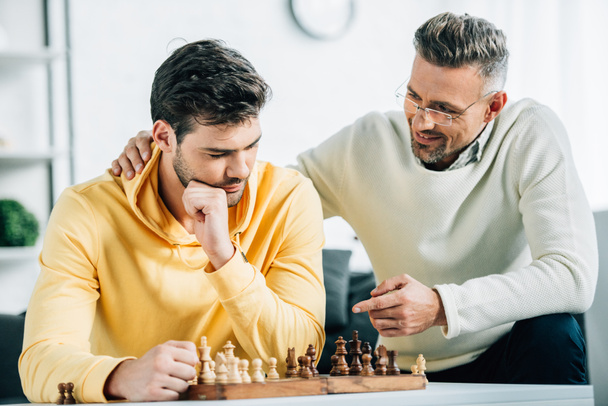 son and mature father playing chess together on weekend at home - Fotó, kép