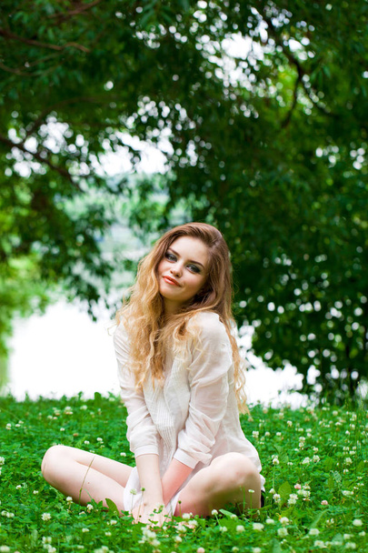 Sexy young blonde woman in white dress sitting on green grass in summer park - Valokuva, kuva
