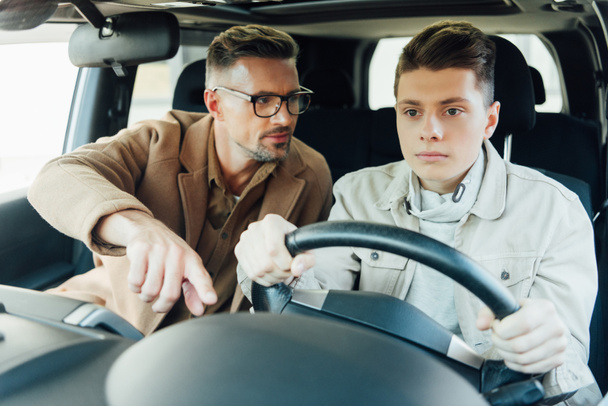 handsome father teaching teen son driving car and pointing on something - Photo, Image