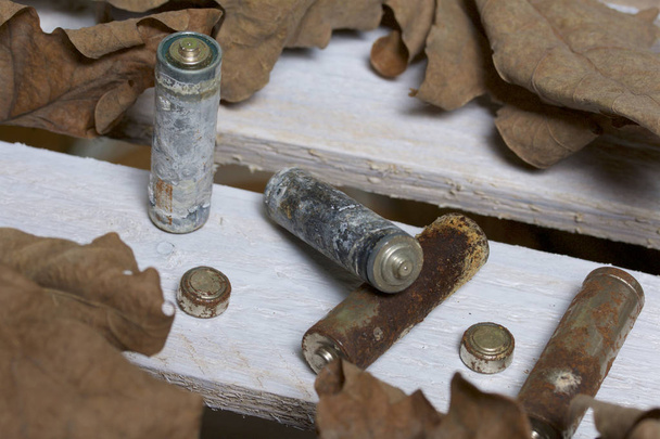 Spent batteries, coated with corrosion. Different shapes and sizes. They lie on a wooden box among the dead autumn leaves. Environmental protection, recycling. - Photo, Image