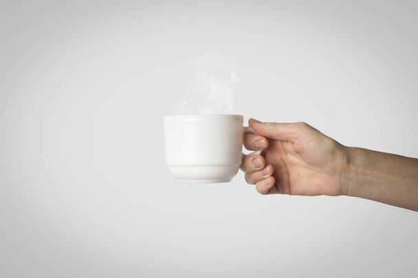 Mano femminile che tiene una tazza bianca con caffè caldo su uno sfondo grigio. Vista laterale
. - Foto, immagini
