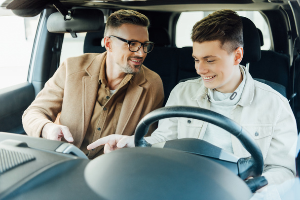 smiling handsome father teaching teen son driving car - Photo, Image