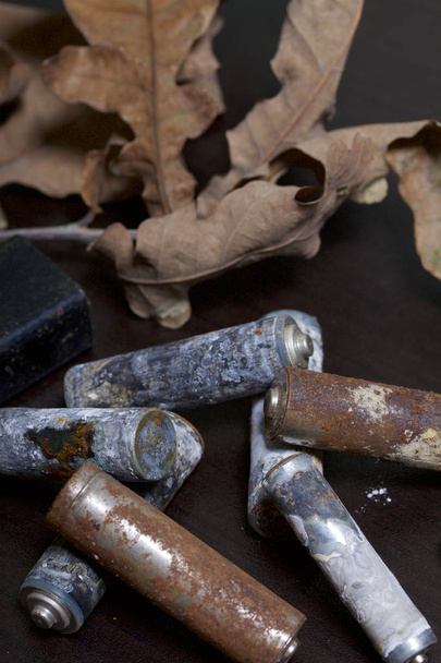 Spent batteries, coated with corrosion. Different shapes and sizes. They lie on a dark background among the dead autumn leaves. Environmental protection, recycling. - Photo, image