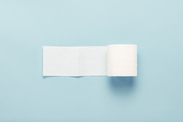 Roll of unfolded toilet paper on a blue background. Flat lay, top view. - 写真・画像