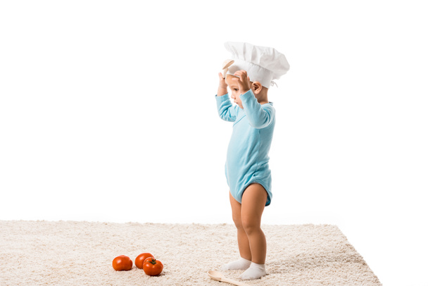 toddler boy in chefs hat standing near fresh tomatoes on carpet isolated on white - Photo, Image