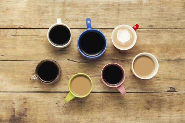 Um monte de copos multicoloridos com café e bebidas de café em um fundo de madeira. Conceito café da manhã com café, café com amigos. Deitado plano, vista superior
. - Foto, Imagem