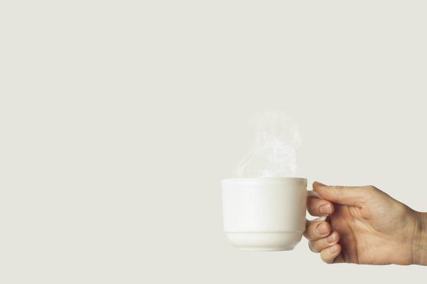 白いカップに灰色の背景にホット コーヒーを持っている女性の手。横から見た図. - 写真・画像