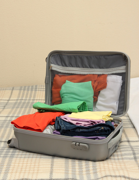 Open grey suitcase with clothing on bed - Foto, immagini
