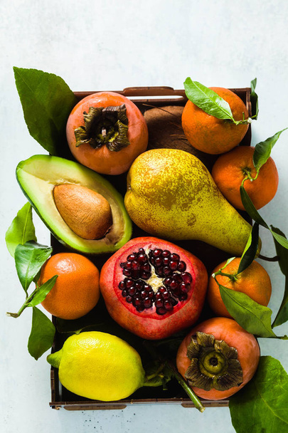 different fruits of pomegranate, pear, mandarin, lemon, avocado and persimmon with coconut on the table. basis of healthy nutrition and daily juices in a wooden box - Photo, image