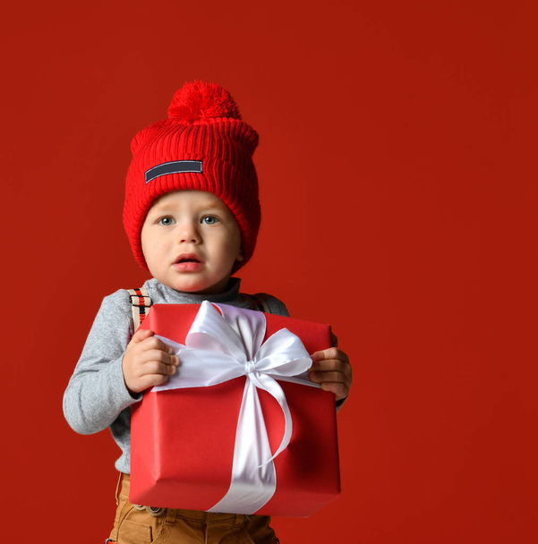 Portrait of a little boy  with a pompon. holding a large gift box with a white bow.  - Fotoğraf, Görsel
