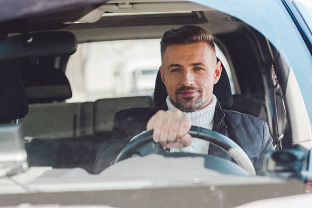 Cheerful man sitting in car and holding steer - Photo, image