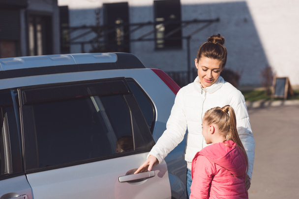 Mother opening car door and standing with daughter on street - Фото, изображение