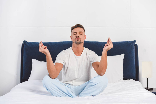 schöner Mann praktiziert Yoga im Pyjama - Foto, Bild