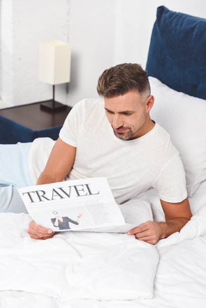 Knappe man reizen krant in bed lezen - Foto, afbeelding