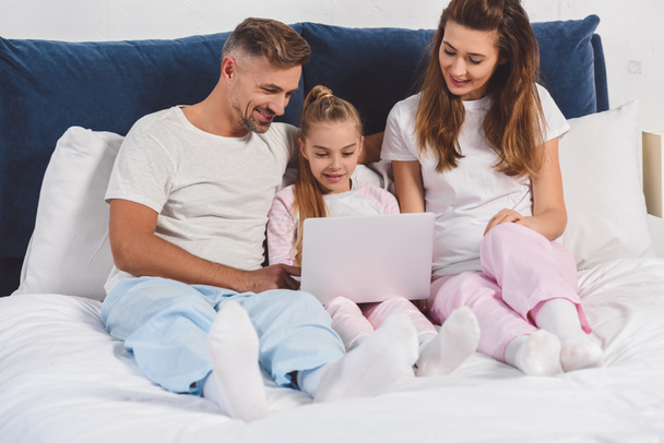 Family lying in bedroom in sleepwear with laptop  - Valokuva, kuva