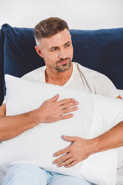 Handsome man holding pillow in room  - Foto, Bild