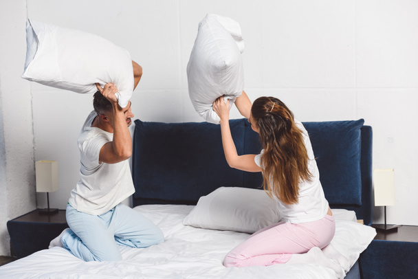 Cheerful couple having pillow fight in bedroom - Fotoğraf, Görsel
