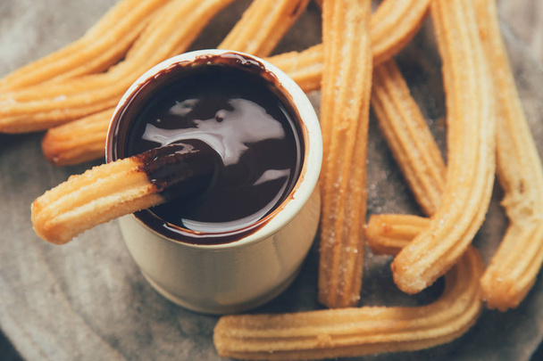 Traditional spanish churros with hot chocolate sauce on a rustic wooden slice. Top view - Photo, Image