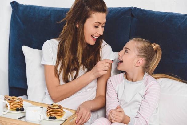 mother feeding daughter in bed during breakfast - Photo, Image