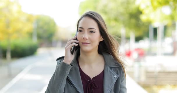 Vooraanzicht van een gelukkige vrouw lopend en pratend op telefoon in een park - Video