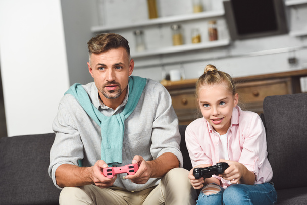 concentrated smiling daughter playing video game with father - Photo, Image