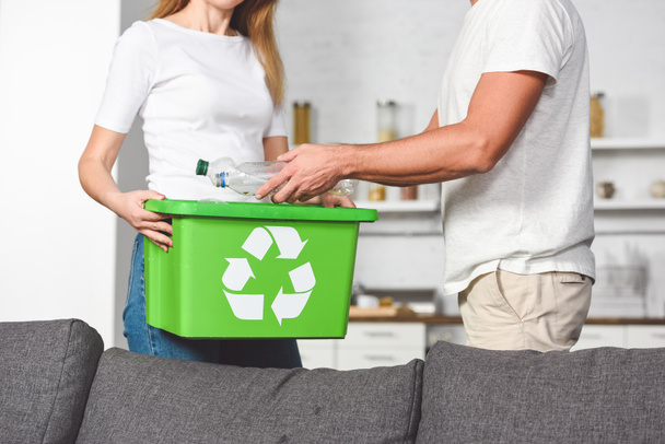 cropped view of adult couple putting empty plastic bottles in recycle green box - Foto, immagini