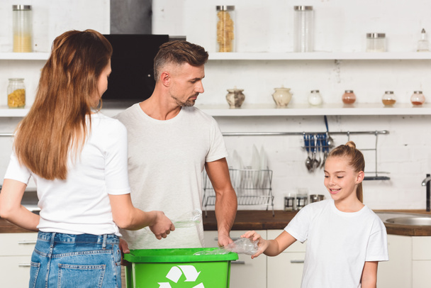 familia de pie en la cocina y poner botellas de plástico vacías en la caja de reciclaje verde
  - Foto, Imagen