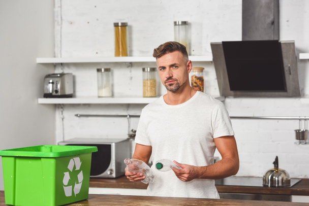 handsome man holding plastic bottles with green recycle box at wooden table - Foto, afbeelding