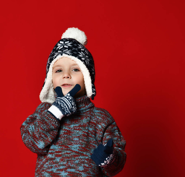 child boy in knitted hat and sweater and mittens having fun over colorful red  background. - Foto, Imagem