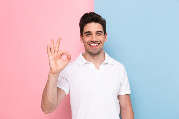 Image of man 30s having stubble showing ok sign with happy smile isolated over colorful background - Zdjęcie, obraz