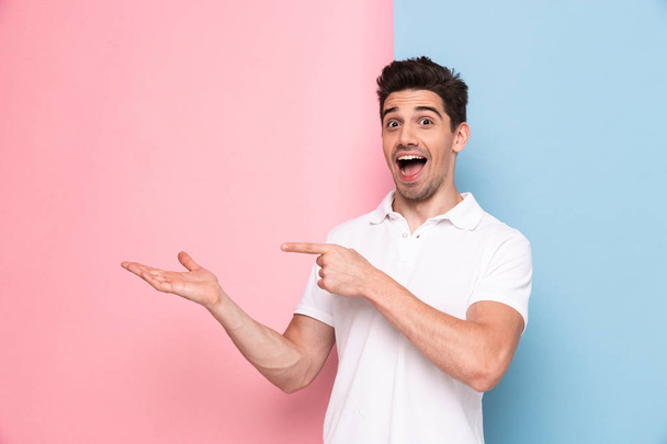 Image of cheerful man 30s having stubble pointing fingers aside at copyspace isolated over colorful background - Fotó, kép