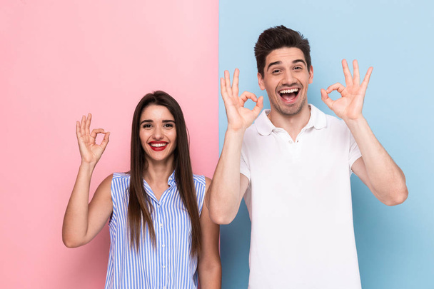 Image of joyful couple in casual wear smiling and gesturing ok sign isolated over colorful background - Foto, immagini