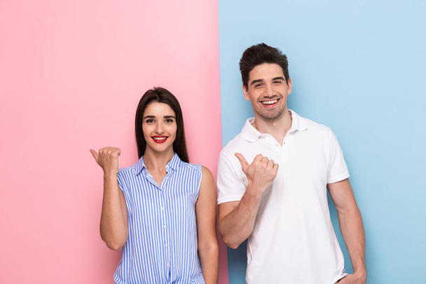 Image of european couple in casual wear smiling and gesturing fingers aside isolated over colorful background - Φωτογραφία, εικόνα