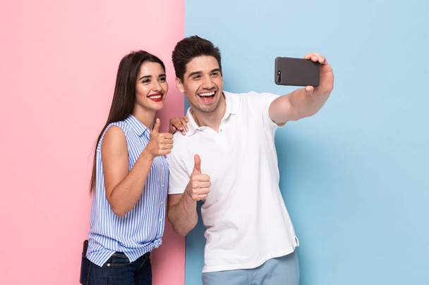 Image of caucasian couple using mobile phone and taking selfie photo isolated over colorful background - Φωτογραφία, εικόνα