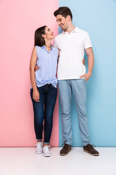 Full length image of attractive man and woman in casual wear hugging and smiling together isolated over colorful background - Фото, изображение