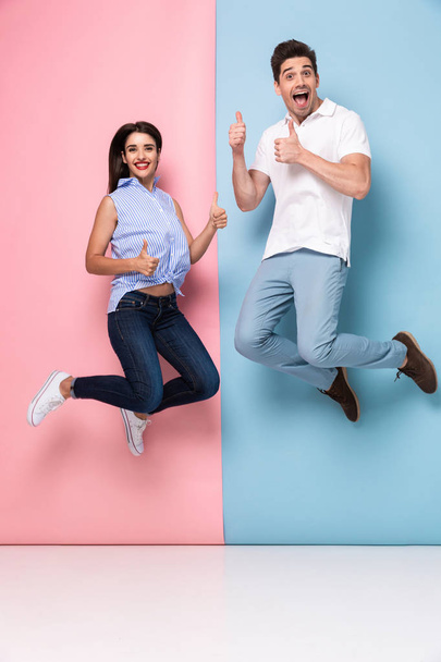 Full length image of cheerful man and woman in casual wear jumping and smiling together isolated over colorful background - Foto, imagen