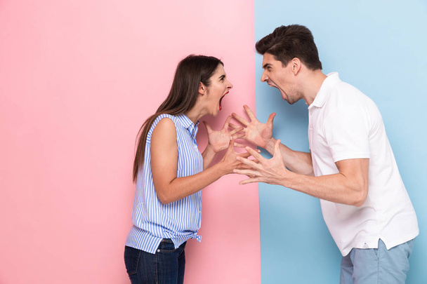 Photo of angry man and woman in casual clothes screaming at each other standing face to face isolated over colorful background - Foto, Imagem